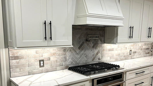 White shaker cabinets with matte black hardware, quartz countertop and brick herringbone backsplash